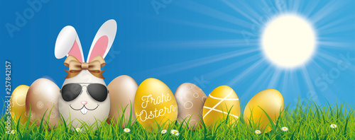 Frohe Ostern Banner mit goldenen Ostereiern im Gras und einem Osterhasen mit Sonnenbrille