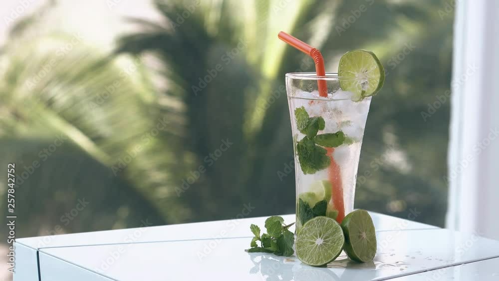 long green palm branches swing smoothly behind white table with limes and frozen beverage with long plastic straw
