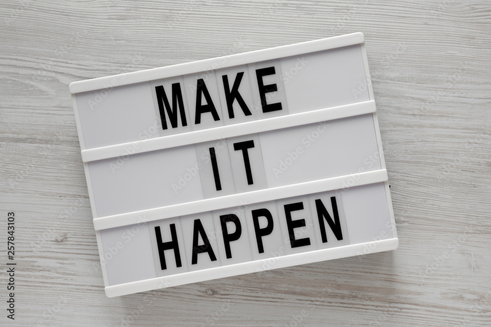 Lightbox with words 'Make it happen' on a white wooden background, top view. From above, flat-lay, overhead.