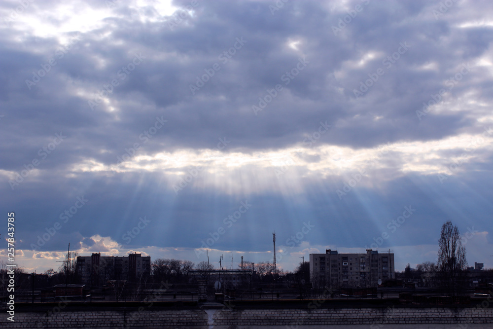 Evening landscape with sunny rays falling from clouds onto city