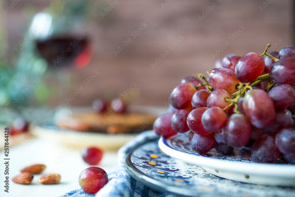 close up blue plate with bunch of red grapes, wine, white table, wooden background close up blue plate with bunch of red grapes, wine, white table, wooden background