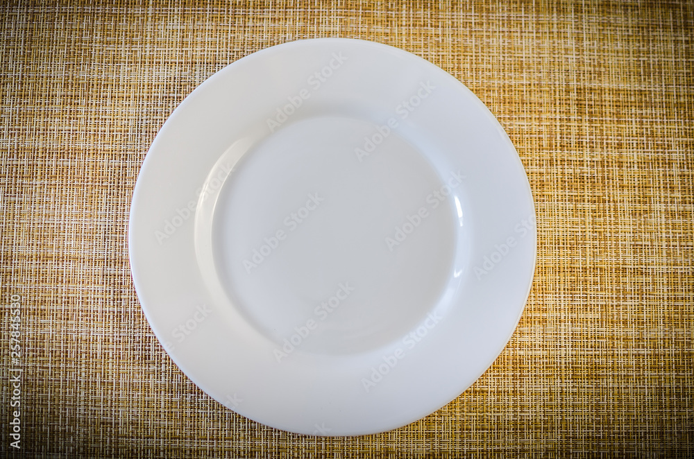 Empty white plate over brocade tablecloth, top view. Empty white plate over brocade tablecloth, top view.
