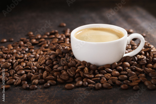 Coffee cup on roasted coffee beans. Dark background, sun rays.
