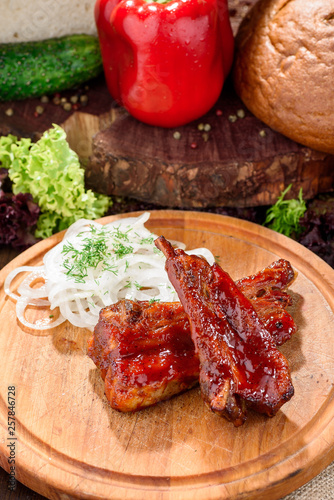 grilled veal ribs on a wooden round board against the background of fresh vegetables. close-up. space