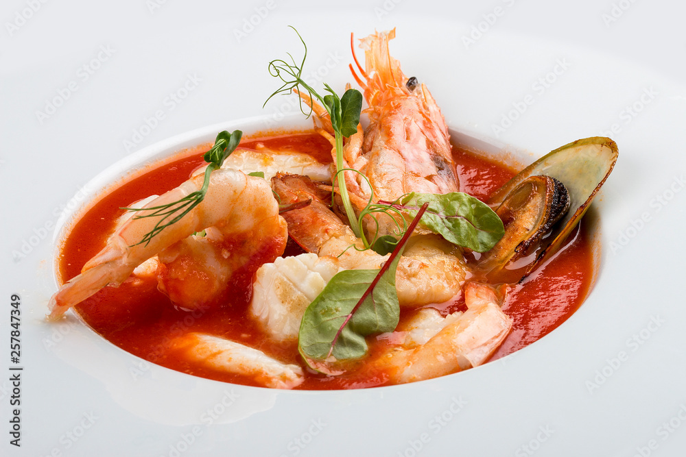French bouillabaisse fish soup with shrimp, mussels and scallop. In a white plate on a textile background French bouillabaisse fish soup with shrimp, mussels and scallop. In a white plate on a textile background