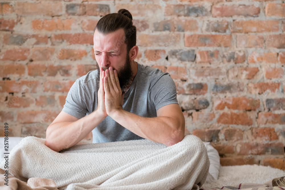 Bad night sleep. Stress and insomnia. Man sitting in bed and yawning widely. Modern loft interior. Copy space. Bad night sleep. Stress and insomnia. Man sitting in bed and yawning widely. Modern loft interior. Copy space.