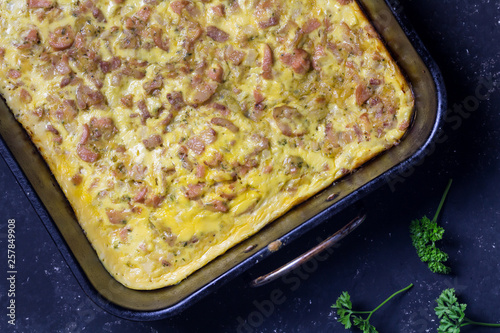 Cheesy bacon and sausage breakfast bake in oven tray on black background - Savory tart