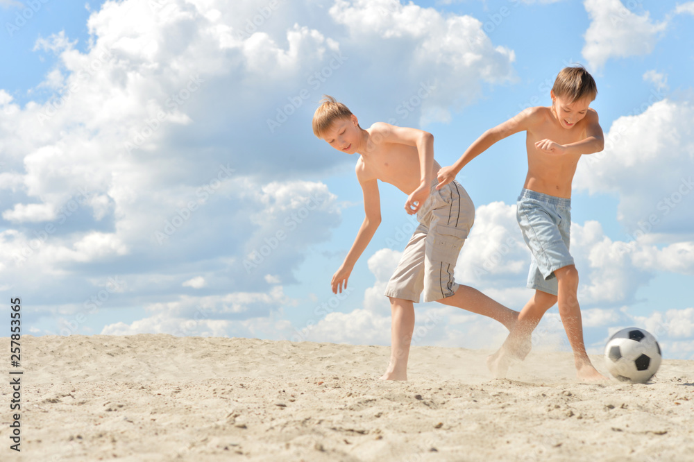 Portrait of two brothers playing football on beach in summer day Portrait of two brothers playing football on beach in summer day
