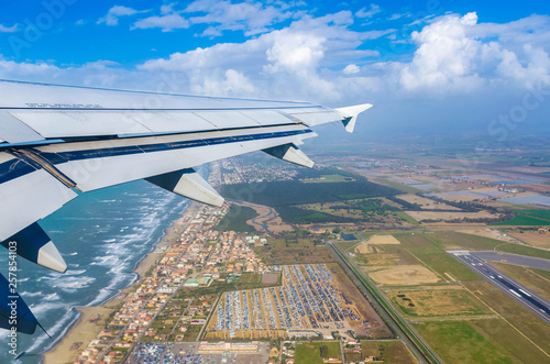 Looking through window aircraft at wing of airplane flying  over the  fiumicino where is situated the Fiumicino International Airport 