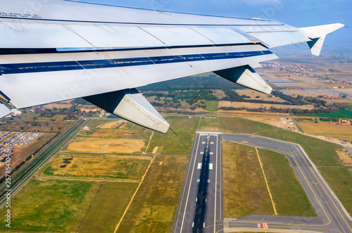 Looking through window aircraft at wing of airplane flying  over the  fiumicino where is situated the Fiumicino International Airport 