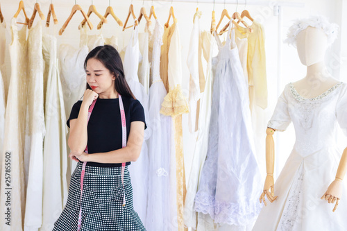 Young Asia working woman. She is standing behind is wedding dress. She is worry and stressed out because of work.She is tailor shop owner.Clothing store,wedding,Photo concept work and fashion. © Teerayut