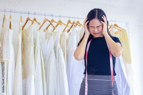 Young Asia working woman. She is standing behind is wedding dress. She is worry and stressed out because of work.She is tailor shop owner.Clothing store,wedding,Photo concept work and fashion.