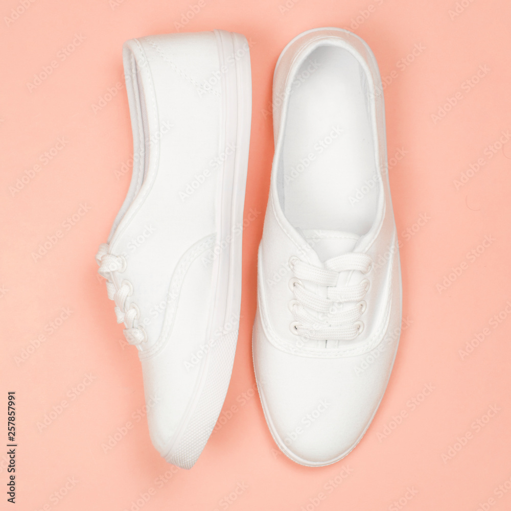 White female sneakers on coral background. Flat lay, top view minimal style White female sneakers on coral background. Flat lay, top view minimal style