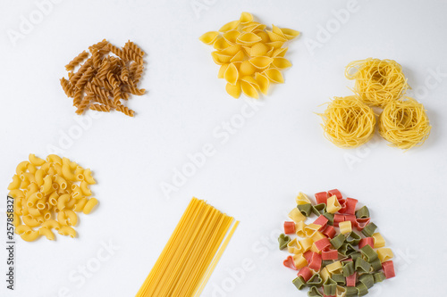 On a white background, various types of pasta: horns, hearts, shells, spaghetti, whole-wheat pasta. Free space for text