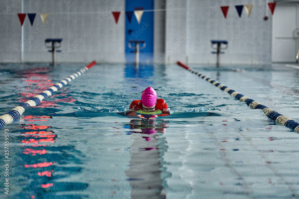 Obraz premium Female athlete in a red-yellow swimsuit is swimming in the style of breaststroke. Splashes of water scatter in different directions.