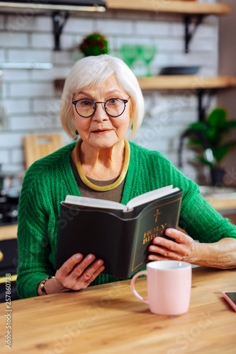 Portrait of lady having seat at kitchen table with Bible