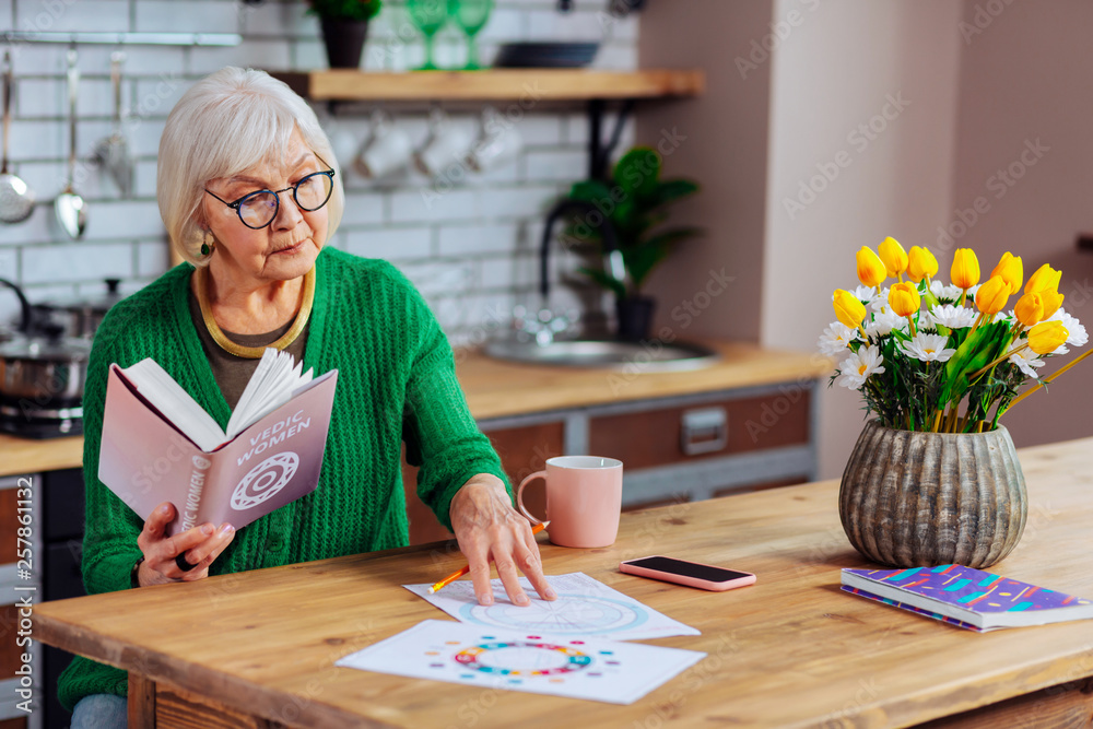 Aging grandmother concernedly looking at vedic drawing at kitchen room Aging grandmother concernedly looking at vedic drawing at kitchen room