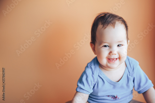 Beautiful small girl or boy with dark hair smiling on a bright orange background colour of 2019 with space for text happy smile look at camera