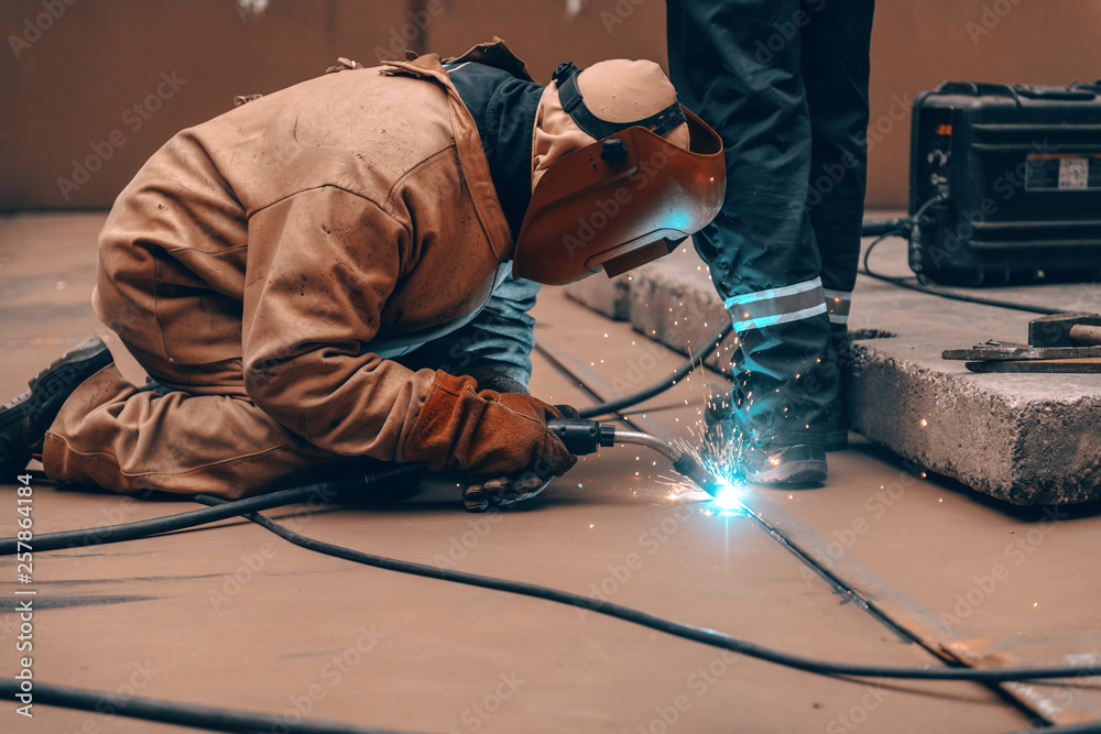Worker in protective suit and mask crouching and welding in metal tower at construction site. Worker in protective suit and mask crouching and welding in metal tower at construction site.