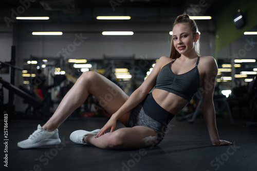 Fitness girl posing in the gym sitting on the floor showing off her body