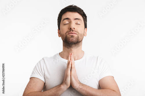 Image of caucasian man 30s with bristle in casual t-shirt holding palms together and praying