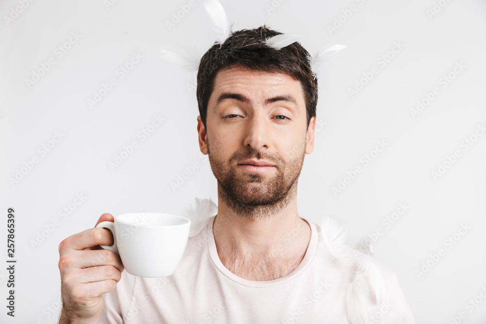 Image of morning man 30s with bristle in casual t-shirt drinking coffee while standing under falling feathers Image of morning man 30s with bristle in casual t-shirt drinking coffee while standing under falling feathers