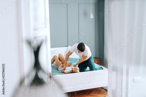 Boyfriend tickling his loving girlfriend in bed. Bedroom interior, morning time.