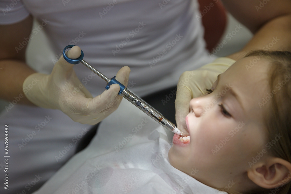 Scared little girl at dentist office, getting local anesthesia injection into gums, dentist numbing gums for dental work.