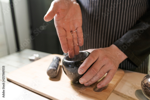 Man chef pounding spices and herbs in mortar for food cooking on a black background