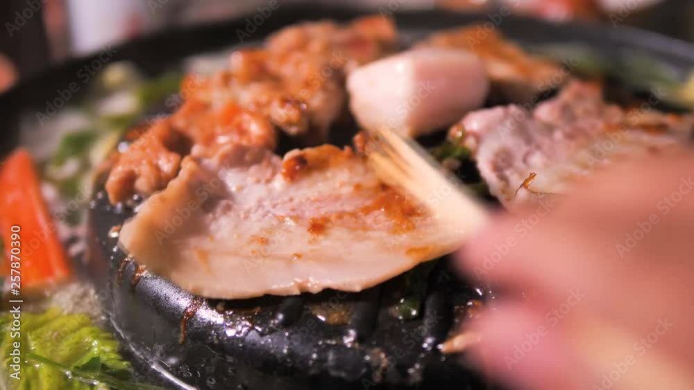 People using chopstick to cooking pick up and flip pork and meet of Korean BBQ barbecue on the hot pot People using chopstick to cooking pick up and flip pork and meet of Korean BBQ barbecue on the hot pot