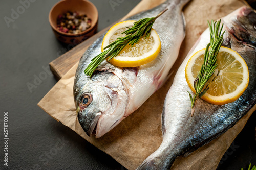 two fresh raw Dorado fish on a cutting board with spices and olive oil on a stone background