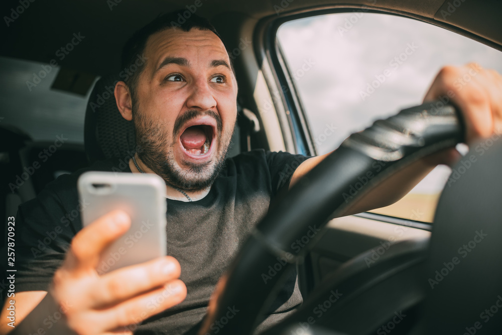 Young man sitting in his car screaming distracted by smartphone Young man sitting in his car screaming distracted by smartphone