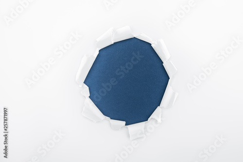 ragged hole in textured white paper on dark blue background