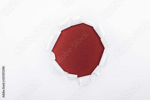 ragged hole in textured white paper on burgundy background