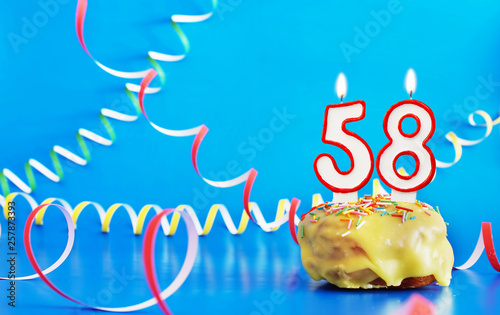 Birthday of fifty eight years. Cupcake with white burning candle in the form of number 58. Vivid blue background with copy space