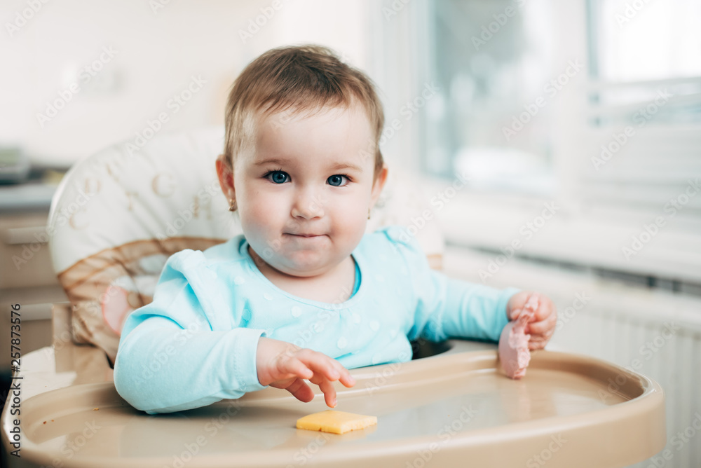 Little girl in a high chair eating cheese Little girl in a high chair eating cheese