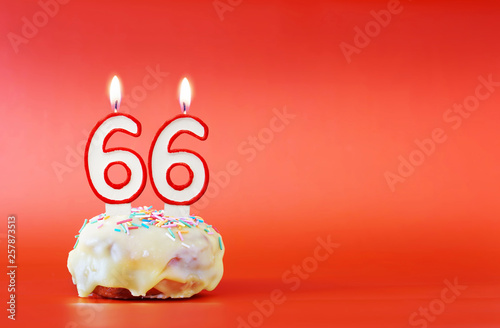 Sixty six years birthday. Cupcake with white burning candle in the form of number 66. Vivid red background with copy space