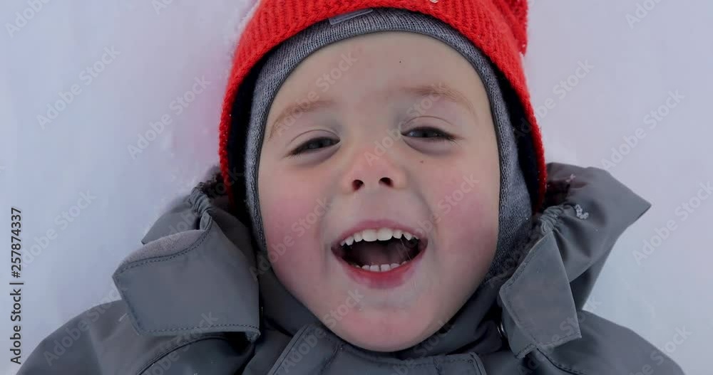 Portrait of a boy close up in winter. The face of the child lying head on the snow. The child opens his mouth