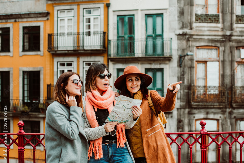 .Three beautiful and funny women traveling together in Porto, Portugal. Standing together carefree and relaxed using their map to locate themselves. Lifestyle. Travel photography