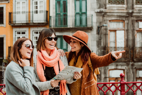 .Three beautiful and funny women traveling together in Porto, Portugal. Standing together carefree and relaxed using their map to locate themselves. Lifestyle. Travel photography