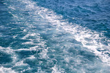 Turbulence made by foam of sea water from a high-speed yacht on surface of sea. Blue sea waves with lot of sea foam. Surface of sea with waves, splash, foam and bubbles, blue background and wallpaper.