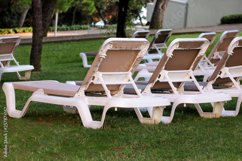 Exotic beach on mediterranean sea, sunbeds for sunbathing and relax on grass in tropical garden of luxury resort hotel. Sun loungers on lawn waiting for tourists. Idyllic seaside in summer season.