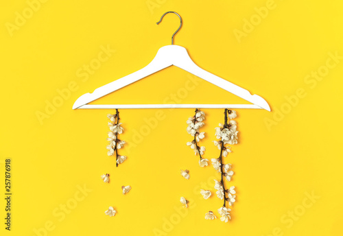 Spring flowering branch hang white wooden hangers on yellow background. Spring sale concept discount store shopping empty hanger promo design. Creative fashion banner. Flat lay top view copy space.