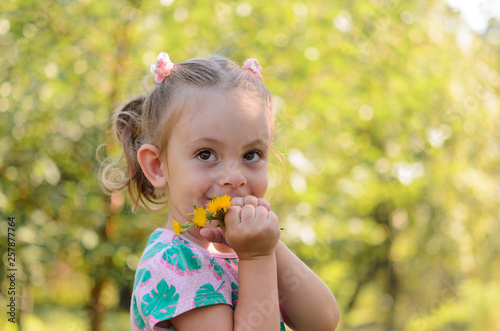 A happy cute little girl with dandelions on a sunny glade.