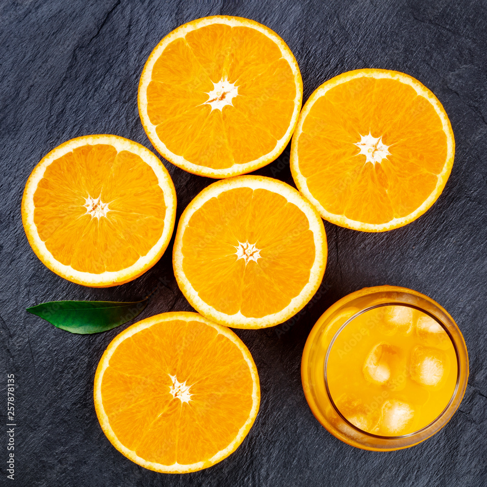 A glass of fresh orange juice with orange halves and a green leaf, shot from above on a black background A glass of fresh orange juice with orange halves and a green leaf, shot from above on a black background