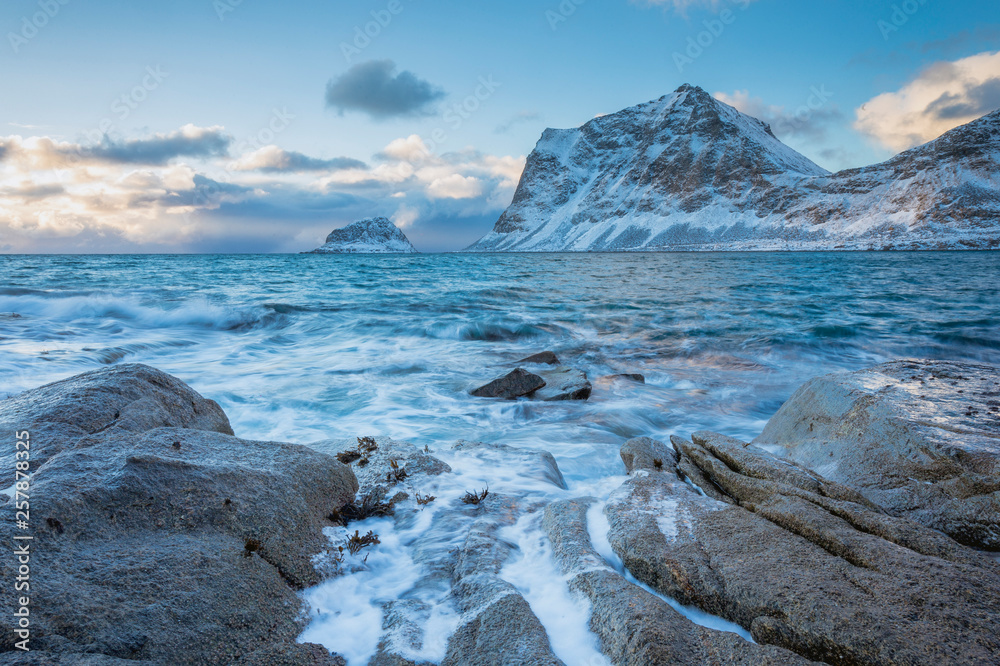 Rocky coast with beautiful mountains and big waves, blue sky in the winter on the Lofoten Islands in Norway