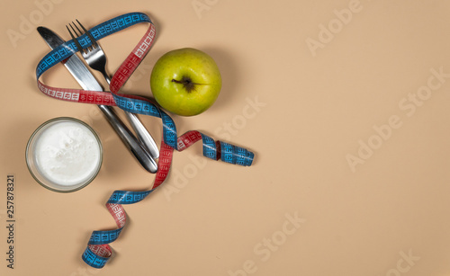 Concept diet - healthy food with apple, yogurt and measuring tape on yellow background. photo