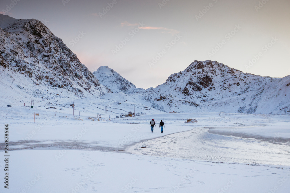 Two tourists are walking along a crystal clear winter beach with mountains on the Lofoten Islands in Norway