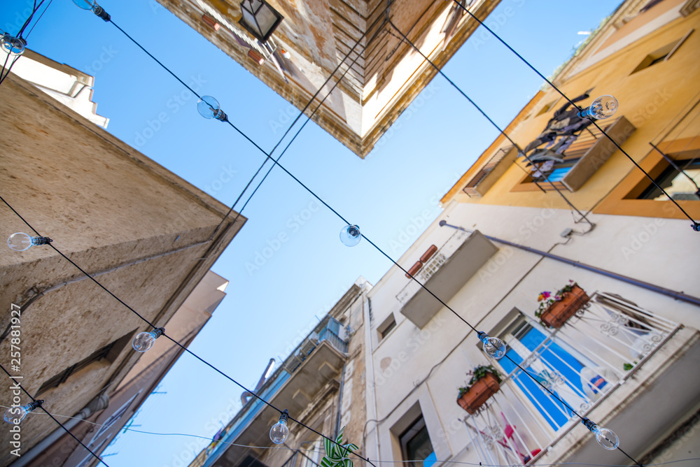 Hanging light bulbs in colorful, romantic, narrow streets of Bari, Italy. Traditional architecture in old town. 