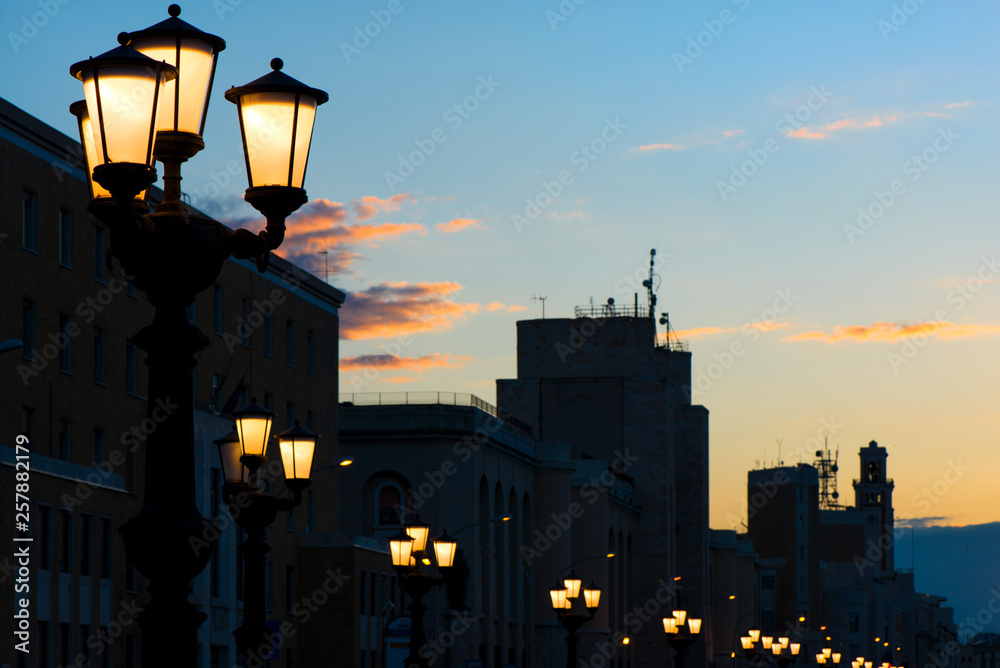 Lamp posts at seafront and promenade in Bari, Italy. Romantic, calm, relaxing evening in city. Sun is setting over old town.